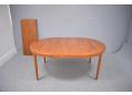 Extendable round dining table with teak top and tapering legs.